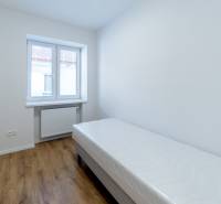 Ein Zimmer mit einem Einzelbett, einem Fenster und einem Boden mit Holzdekor in einer 3-Zimmer-Wohnung.