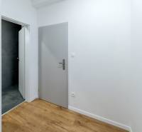 Ein Flur mit grauen Türen, einem Badezimmer mit dunklen Fliesen und einem Boden in Holzoptik.