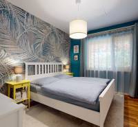 Schlafzimmer in einem Einfamilienhaus mit Palmen auf der Tapete, Holzboden und weißen Möbeln.