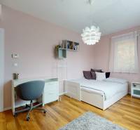 Schlafzimmer in einem Einfamilienhaus mit Schreibtisch, Bett und Boden in Holzoptik.