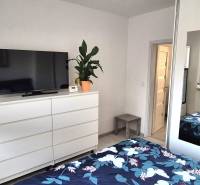 Schlafzimmer in einer 2-Zimmer-Wohnung mit weißen Möbeln, Spiegel und Fernseher auf der Kommode.