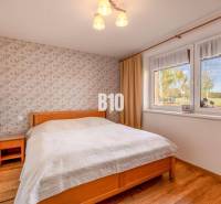 Ein Schlafzimmer in einem Einfamilienhaus mit einer geblümten Tapete und einem Boden in Holzoptik.