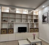 Ein Wandschrank mit Regalen und Dekorationen in einer Zweizimmerwohnung, daneben ein Tisch mit Blumen.