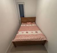 Schmales Schlafzimmer in einer 2-Zimmer-Wohnung mit einem Holzbett und einer Blumenbettdecke.