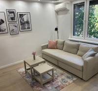 Obývačka v 2-izbovom byte, s pohovkou, stolíkmi a fotografiami na stene.