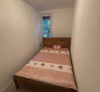 Schmales Schlafzimmer mit einem Bett mit gemustertem rosa Überwurf in einer Zweizimmerwohnung.
