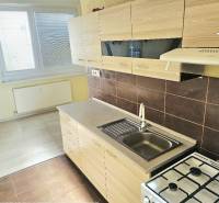 Küche in einer 2-Zimmer-Wohnung mit weißen Schränken und einem Boden in Holzoptik.