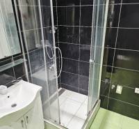Badezimmer in einer 2-Zimmer-Wohnung mit Dusche und Waschbecken, schwarze Fliesen.