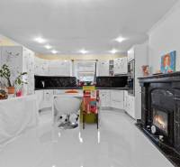 Küche in einem Einfamilienhaus mit Kamin, weißen Schränken und Pflanzen, Boden mit Holzdekor.