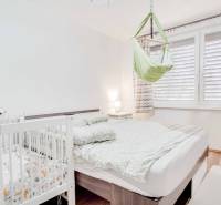 Schlafzimmer in einer 3-Zimmer-Wohnung mit Bett, Kinderbett und Schaukel, Boden mit Holzdekor.