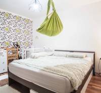 Schlafzimmer mit gemusterten Tapeten und grünem Schaukelstuhl in einer 3-Zimmer-Wohnung.