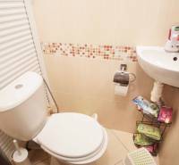 Badezimmer mit Toilette und Waschbecken in einer 3-Zimmer-Wohnung, beige Fliesen.