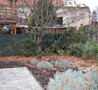 Garten bei einem Einfamilienhaus in Nitra, mit Bäumen, Stauden und gepflasterter Fläche.