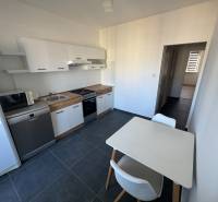 Küche in einer 3-Zimmer-Wohnung mit weißen Schränken und Tisch, auf dunklem Boden.