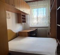 Schlafzimmer in einer 3-Zimmer-Wohnung mit Bett, Schränken und Fenster mit Spitzenvorhängen.