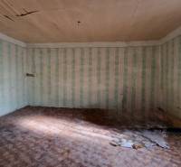 Ein Zimmer in einem Einfamilienhaus mit beschädigter Decke, Tapeten und einem Boden mit Holzdekor.