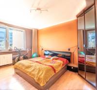 Schlafzimmer mit orangefarbener Wand, Bett und Boden mit Holzdekor in einer 3-Zimmer-Wohnung.