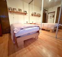 Schlafzimmer in einer 3-Zimmer-Wohnung mit Bett, Spiegelschrank und Boden mit Holzdekor.