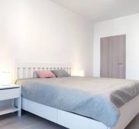 Schlafzimmer mit Bett, Nachttisch und Boden mit Holzdekor in einer 2-Zimmer-Wohnung.