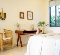 Helles Schlafzimmer in einem Einfamilienhaus mit einem Rattansessel und einem Holztisch.