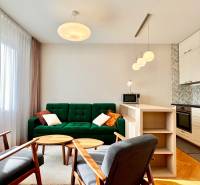 Helles Wohnzimmer mit Küche, grünes Sofa, Holzelemente, drei Lampen.