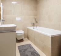 Badezimmer in einer Einzimmerwohnung mit Badewanne, Waschmaschine und Toilette in neutralen Tönen.