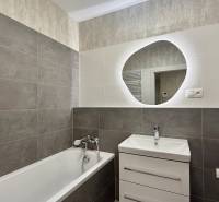 Badezimmer in einer 2-Zimmer-Wohnung mit Badewanne und Waschbecken, helle und dunkle Fliesen.