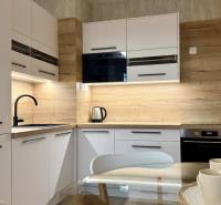 Küche in einer 2-Zimmer-Wohnung mit weißen Schränken, schwarzem Spülbecken und Boden in Holzoptik.