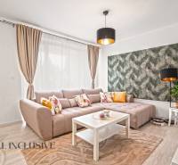 Wohnzimmer mit beigem Sofa, weißem Tisch und Tapete mit Naturmotiv.