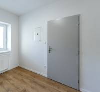 Ein Zimmerinterieur mit weißen Wänden, einem Boden in Holzoptik und einem Fenster.