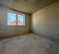 Izba v rodinnom dome, steny bez dekorácií, vidno strechu susednej budovy.