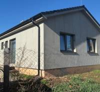 Ein Einfamilienhaus in Tesárske Mlyňany mit grauer Fassade und Fenstern, eingezäunt mit einem Maschendrahtzaun.