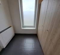 Ein Büro mit Fliesenboden, Stauraum und einem großen Fenster, ohne Möbel.