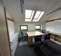 Ein Büro mit einem Boden in Holzoptik, Dachfenstern und Tischen mit Stühlen.