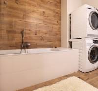 Badezimmer mit Badewanne, Waschmaschine, Trockner und Wand mit Holzdekor in einer 3-Zimmer-Wohnung.