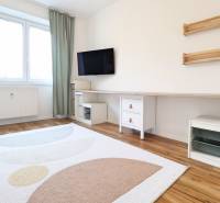 Ein Zimmer in einer 3-Zimmer-Wohnung mit Fernseher, weißen Möbeln und einem Boden in Holzoptik.