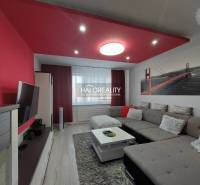 Wohnzimmer in einer 3-Zimmer-Wohnung mit Sofa, Fernseher und roten Dekorationen.