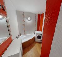 Badezimmer in einer 3-Zimmer-Wohnung mit orange-weißen Fliesen, Badewanne und Waschmaschine.