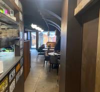 Innenraum von Gastronomiebereichen mit Tellern auf einem Regal, Tafeln, Tischen und Stühlen.