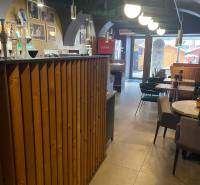 Innenraum von Gastronomiebereichen mit einer Holzbar und Tischen. Auch dekorative Beleuchtung ist zu sehen.