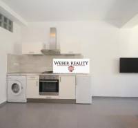 Küche in einer 2-Zimmer-Wohnung mit weißer Küchenzeile, Waschmaschine und Fernseher an der Wand.