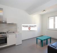 Küche in einer 2-Zimmer-Wohnung mit grauem Boden, Küchenzeile und Sitzgelegenheiten.