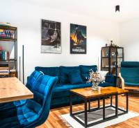 Wohnzimmer einer Zweizimmerwohnung mit einem blauen Sofa, einem Bücherregal und einem Boden in Holzoptik.