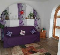 Wohnzimmer eines Einfamilienhauses mit einem Bogenfenster, einem Boden in Holzoptik und einem lila Sofa.