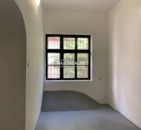 Ein schmaler Raum mit weißen Wänden, ein Fenster mit Gitter, ein grauer Boden im Büro.