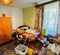 Ein Raum im Einfamilienhaus mit Unordnung, alten Möbeln und einem Ausblick durch das Fenster.