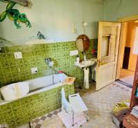 Badezimmer eines Einfamilienhauses mit Badewanne, grünen Fliesen und einem Regal mit Kosmetik.