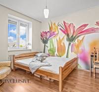 Ein Schlafzimmer in einem Einfamilienhaus mit einer farbenfrohen Blumen-Tapete und einem Boden in Holzoptik.