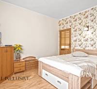 Ein Schlafzimmer in einem Einfamilienhaus mit einer Blumentapete, einem Fernseher und einem Boden in Holzoptik.