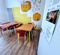 Kinderecke mit bunten Tischen, Stühlen und einem Holzboden in einem Büro.